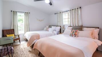 A hotel room with two beds, a desk, a chair, and a ceiling fan.