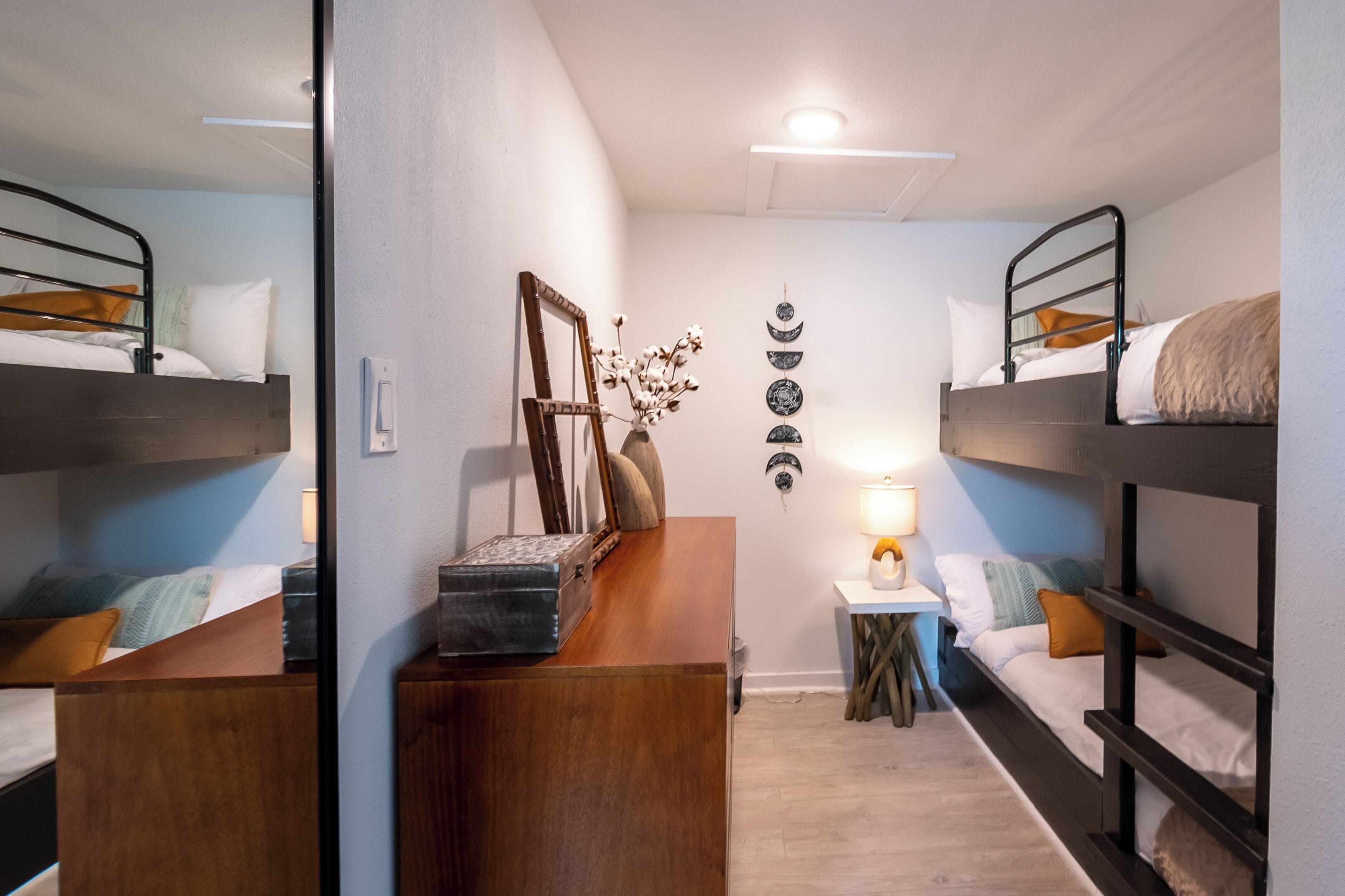 A room with bunk beds, a wooden dresser, a mirror, and a small table with a lamp.