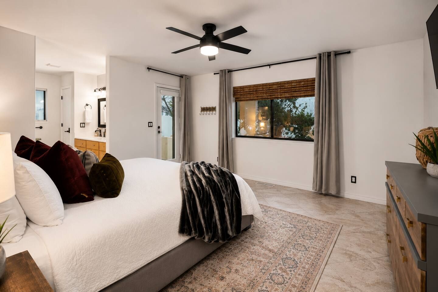 Una camera da letto moderna con un letto grande, una ventola a soffitto, vista sull'esterno e un comò in legno.
