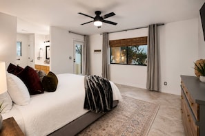 Un dormitorio moderno con una cama grande, un ventilador de techo, vistas al exterior y un aparador de madera.