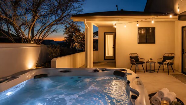 Un jacuzzi con vistas a un atardecer, un patio con sillas y una guirnalda de luces.