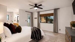 Un dormitorio moderno con una cama, un ventilador de techo, una ventana con cortinas y vistas al exterior.