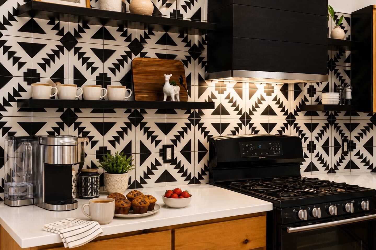 A kitchen with a patterned backsplash, a coffee maker, a stove, and a bowl of strawberries.
