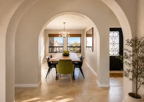 An arched dining area with a chandelier, a wooden table, and chairs.