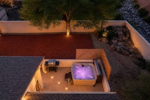 Una terraza en la azotea con jacuzzi, mobiliario de exterior e iluminación con luces colgantes.