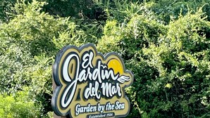 En skylt för ”El Jardín del Mar” med en sol- och havsmotiv, etablerad år 1924, omgiven av grönska.