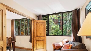 A cozy room with a wooden door, a sofa with a blanket, a small table, and a window with curtains.