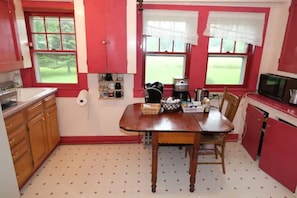 A kitchen with a wooden table, chairs, a microwave, and a window with a view of greenery. - Historic 1874 Farm House at Foot of Gunks (Wallkill)