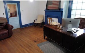 Una stanza con una scrivania in legno, una poltrona in pelle e un computer. Si nota una porta blu e una bandiera americana appesa al muro.