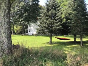 A grassy area with a hammock, a white building, and trees. - Historic 1874 Farm House at Foot of Gunks (Wallkill)