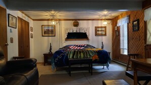 Un dormitorio con una cama, un banco de madera, un sillón de cuero, una mesa de madera y un ventanal con persianas.