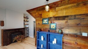 Quarto com parede de madeira, lareira e prateleiras com objetos decorativos.