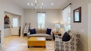 A living room with a sofa, ottoman, patterned armchair, and a chandelier.