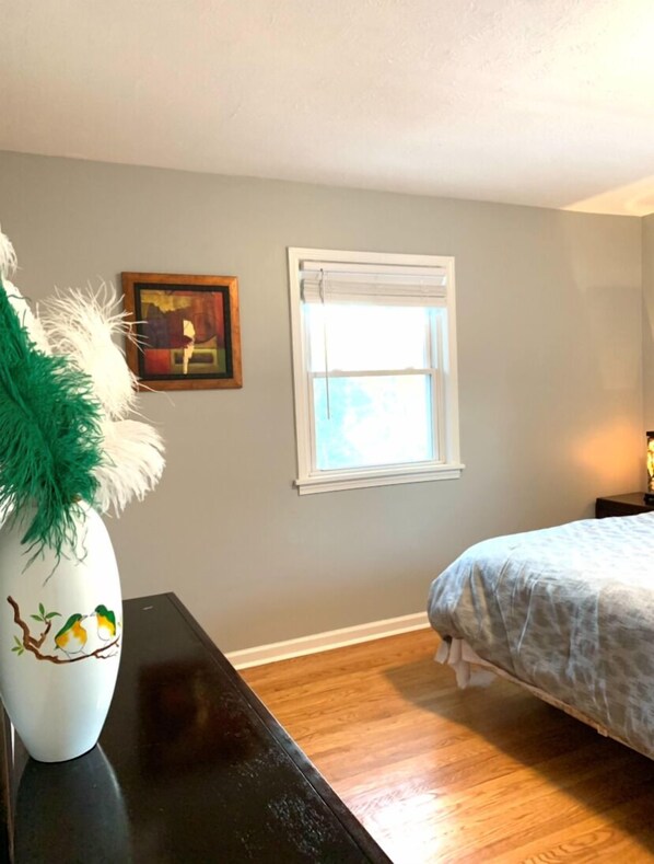 Une chambre à coucher avec un lit, une fenêtre, un tableau et un vase contenant des plumes vertes.
