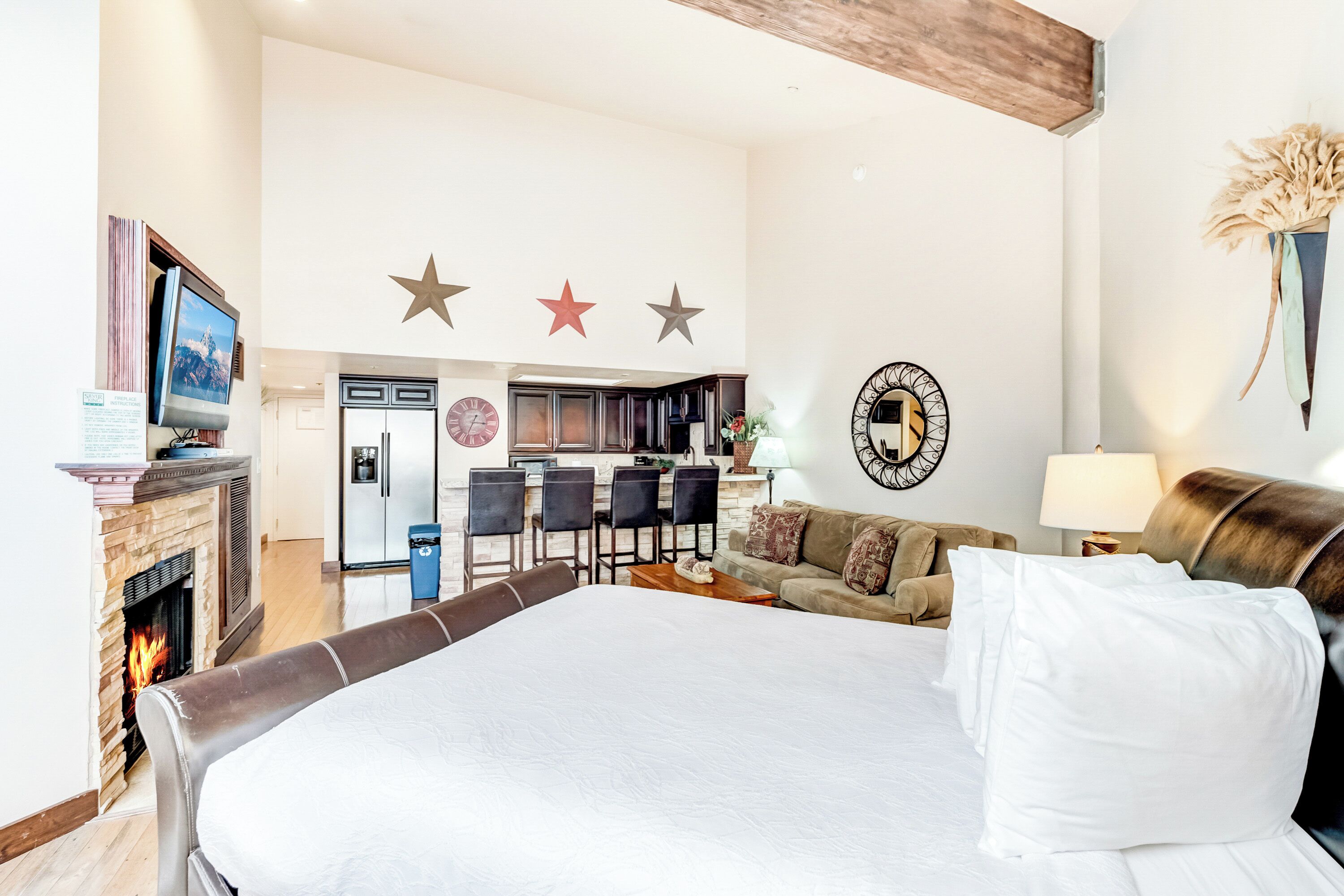 Habitación de hotel con una cama grande, chimenea, zona de comedor con sillas y una cocina al fondo.