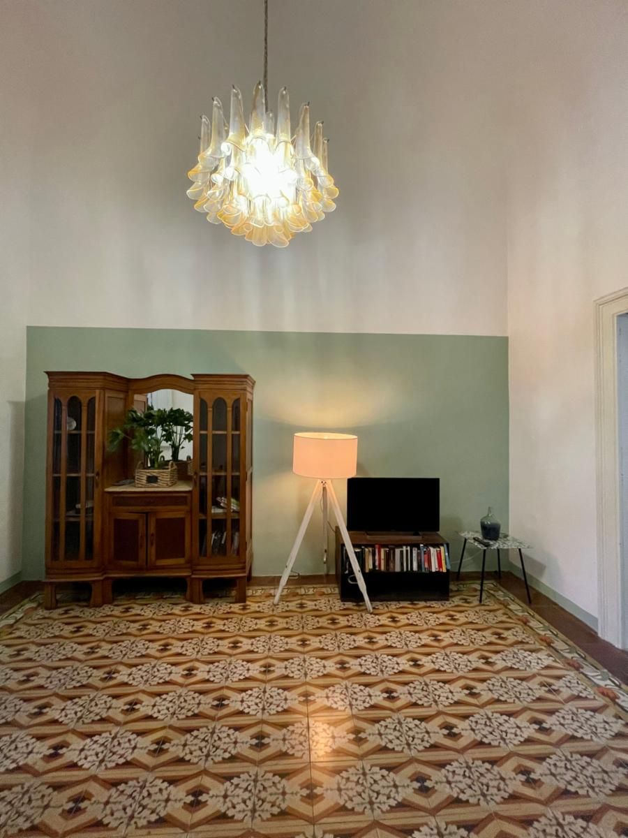 Ein Zimmer mit gemustertem Boden, einem Holzkasten, einer Stehlampe und einem Fernseher.