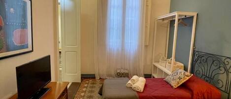 A bedroom with a bed, a TV, a dresser, a window with curtains, and a mirror on the wall.