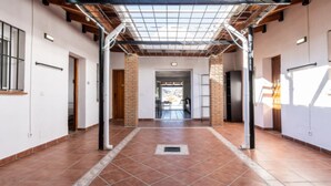 Un pasillo con suelo de baldosas, pilares de ladrillo y estructura de techo metálico.
