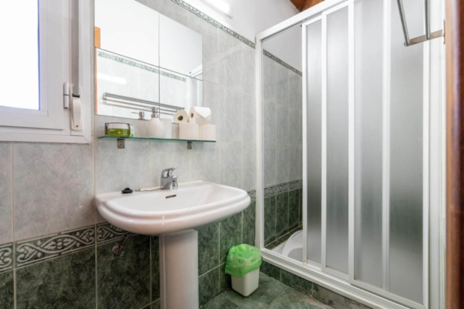 Een badkamer met een witte wastafel, een spiegel en een douche met ruitverdelende glazen deuren.