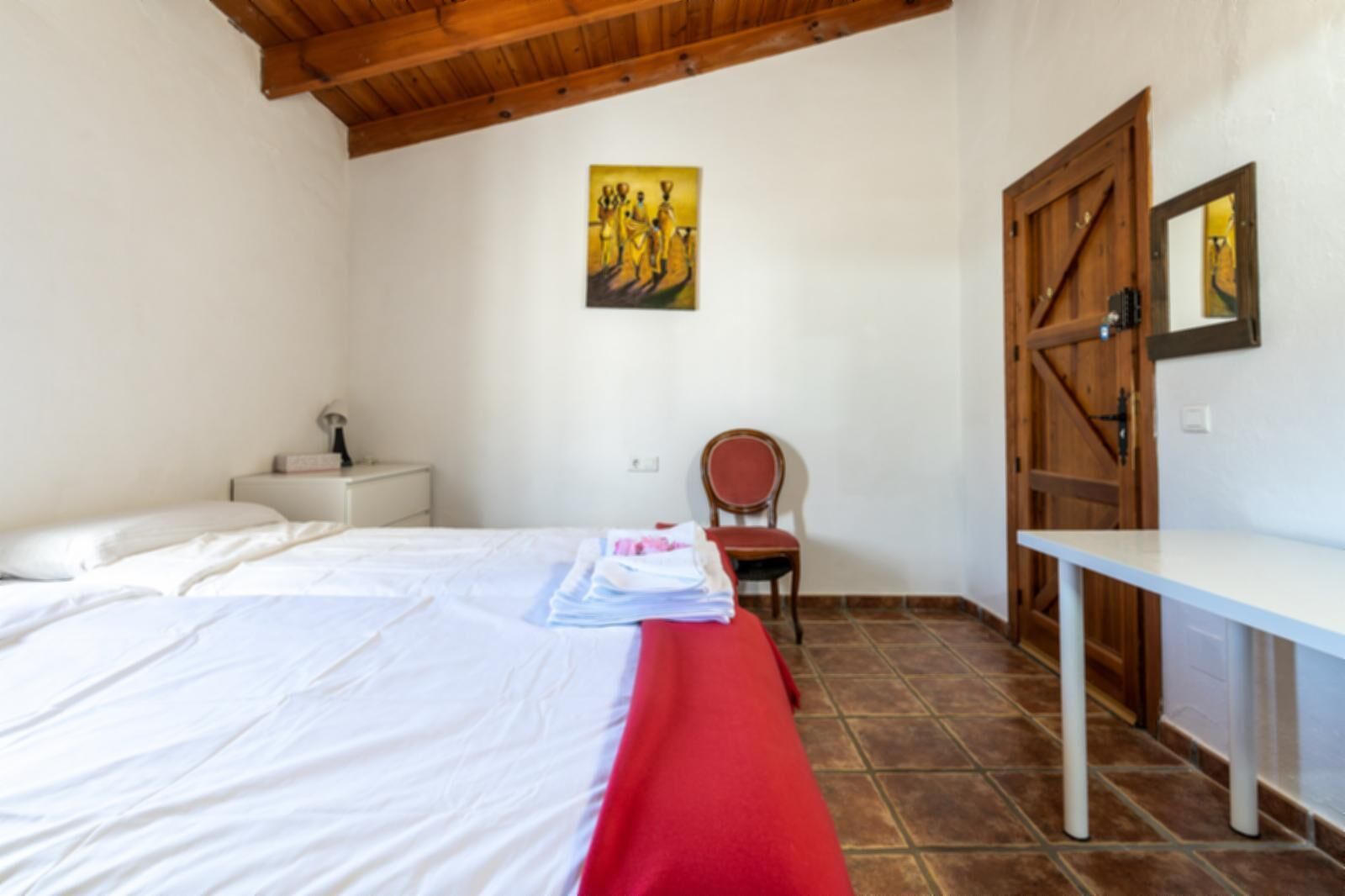 Un dormitori amb un llit, un escriptori, una cadira, un armari de fusta i un quadre a la paret.