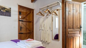 Un dormitorio con cama, armario de madera, espejo y un tendedero con ropa.
