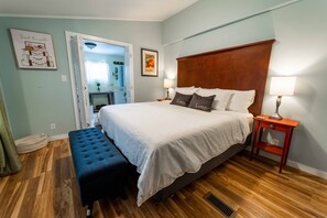 Quarto com cama, duas mesas de cabeceira, um banquinho e porta para outro cômodo.