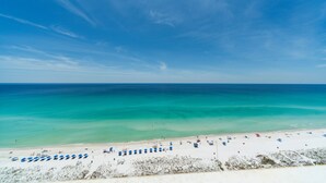 Ein Strand mit weißem Sand, klarem türkisblauem Wasser und wolkenlosem Himmel.