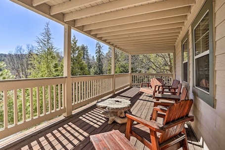 A covered outdoor seating area with wooden chairs and a central table, overlooking a forested landscape.