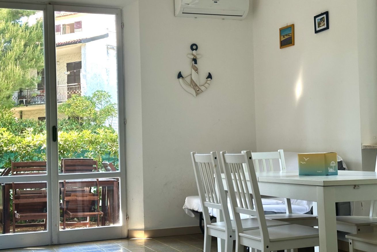 A room with a sliding glass door leading to an outdoor area, a white table with chairs, and a small wall-mounted decoration.