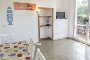 A room with a dining table, a wall-mounted TV, a bookshelf, and a large window.