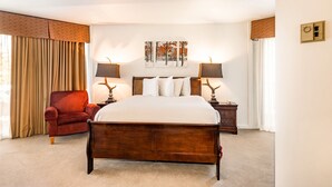 A hotel room with a large bed, a red armchair, two bedside tables with lamps, a painting on the wall, and a window with curtains. - Silver King 203 | 150 Yards to Lifts | Fireplace | Kitchen | End Unit | Mtn View | Pool & Hot Tub (Park City)