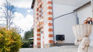 Un edificio con fachada de ladrillo y sección superior blanca, una estatua de piedra en primer plano y un cielo despejado.