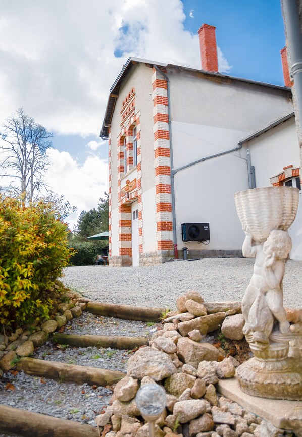 Un edificio con fachada de ladrillo y sección superior blanca, una estatua de piedra en primer plano y un cielo despejado.