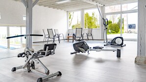 Un gimnasio con diversos equipos de ejercicio, ventanas amplias y un techo alto.