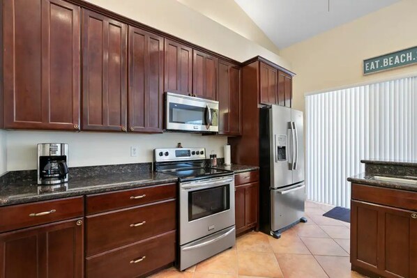 A kitchen with dark wooden cabinets, stainless steel appliances, and a sign that reads "EAT.BEACH." - Singer Island Beach Oasis: Heated Pool, Privacy Fence & Open Concept (West Palm Beach)