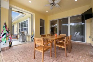 Une terrasse avec une table et des chaises, un ventilateur de plafond et une porte-fenêtre coulissante donnant sur un espace extérieur abrité.
