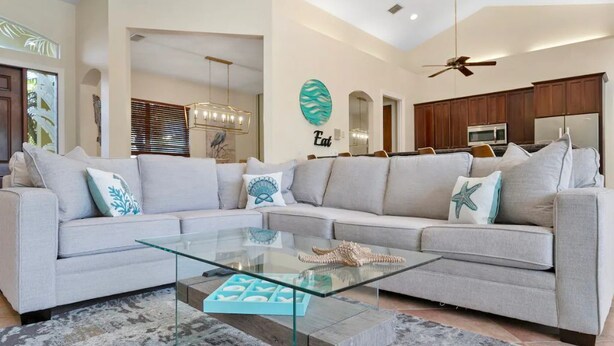 A modern living room with a sectional sofa, a glass coffee table, and a kitchen in the background. - Singer Island Beach Oasis: Heated Pool, Privacy Fence & Open Concept (West Palm Beach)