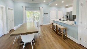 A modern kitchen with a long wooden table, white chairs, and a bar area with stools. - Fabulous 4 bedroom house in North Myrtle Beach (North Myrtle Beach)