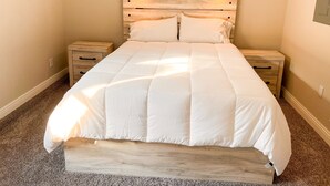 Une chambre à coucher avec un grand lit, deux tables de chevet, une tête de lit en bois et une fenêtre située au-dessus du lit.
