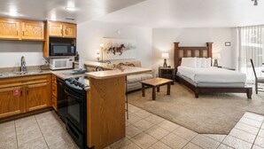 A compact hotel room with a kitchenette, a bed, a small sofa, and a dining table.