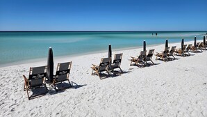 A beach with rows of beach chairs and umbrellas, a clear blue sky, and calm ocean waters. - Castaway Cottage- Lakefront & golf cart included! (Miramar Beach)