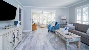 A spacious living room with a large television, a sofa, a patterned armchair, and a coffee table. - Castaway Cottage- Lakefront & golf cart included! (Miramar Beach)