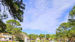 A wooden deck with chairs and tables overlooking a calm lake, surrounded by trees and a clear sky. - Castaway Cottage- Lakefront & golf cart included! (Miramar Beach)