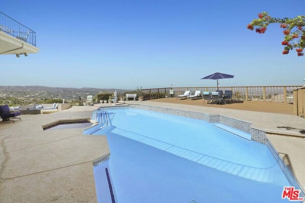 Relax by the rectangular pool surrounded by lounge chairs and umbrellas.