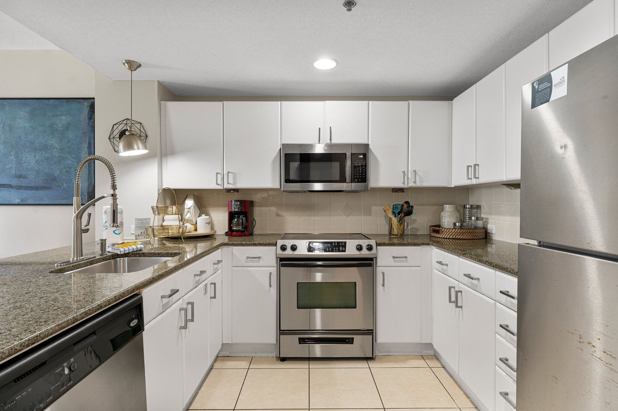 A modern kitchen with white cabinets, stainless steel appliances, a granite countertop, and a dishwasher.