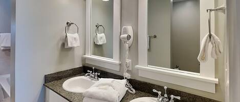 A bathroom with two sinks, a hairdryer, and a towel rack.
