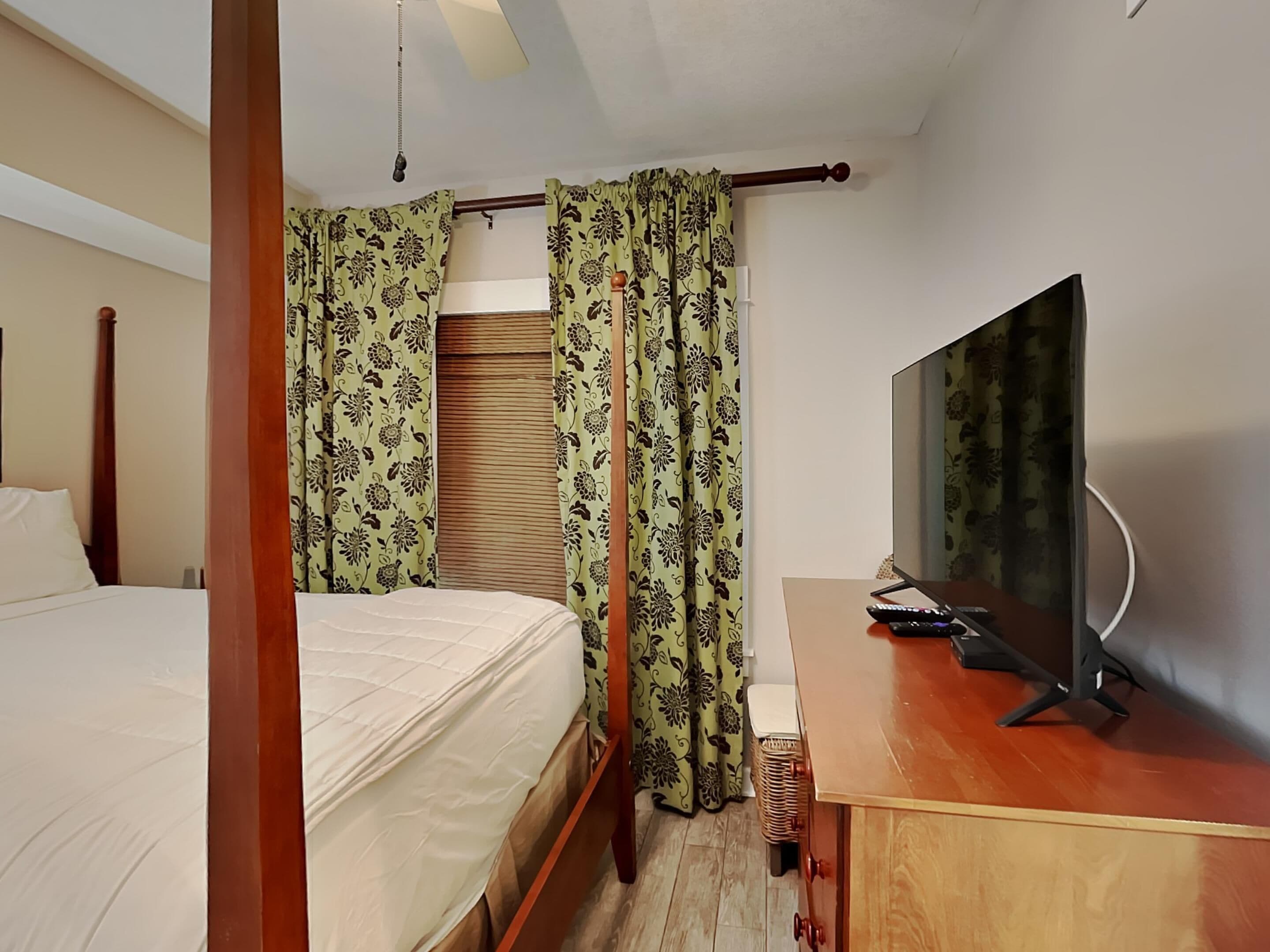 Une chambre d’hôtel avec un lit, un bureau avec une télévision et des rideaux.