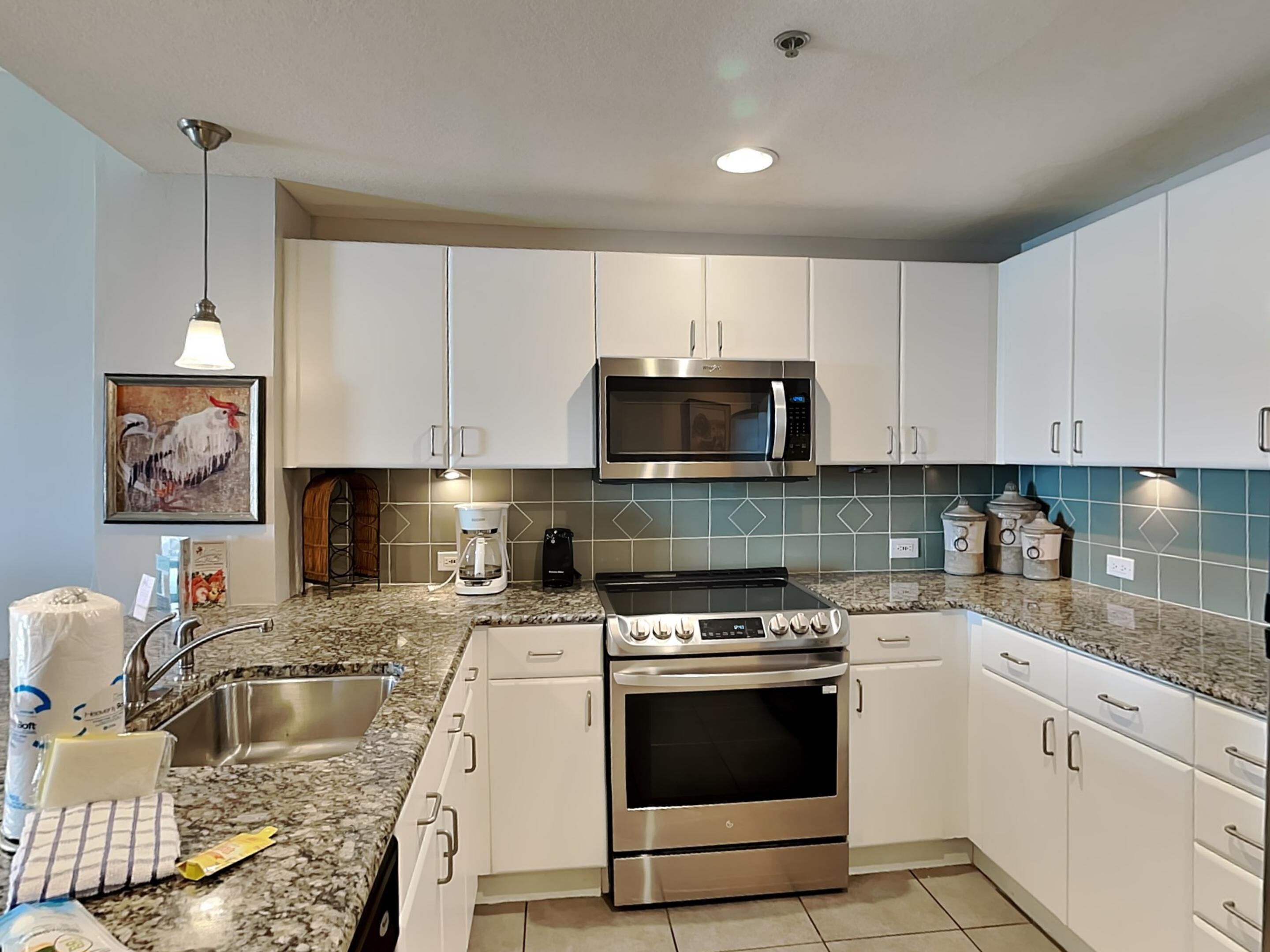 A modern kitchen with white cabinets, a stainless steel stove, a microwave, and a coffee maker.