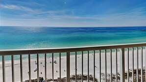A beach view from a balcony with a railing, clear sky, and calm sea.
