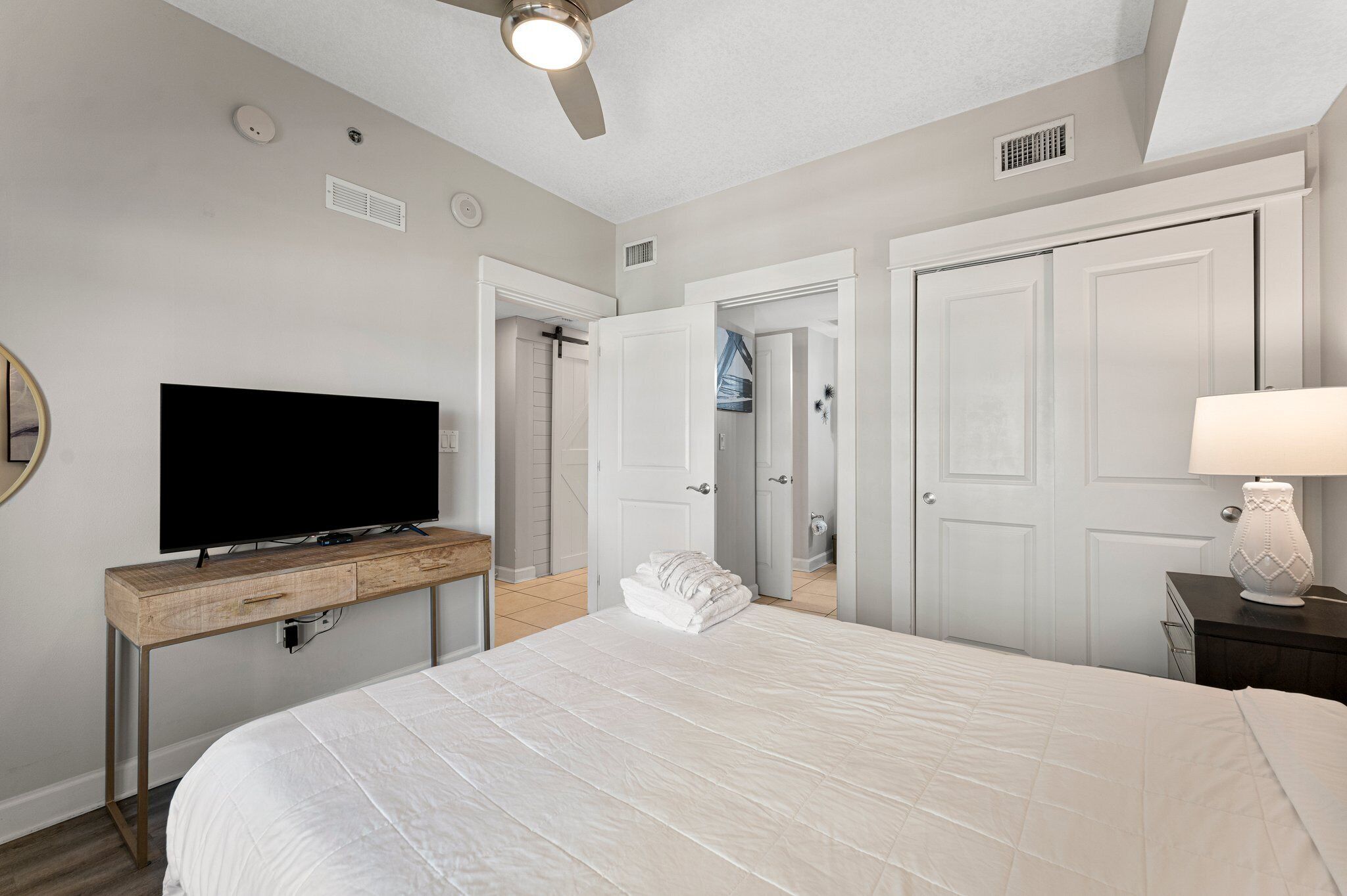 Une chambre d’hôtel avec un lit, un téléviseur posé sur une console en bois, un ventilateur de plafond et des portes blanches.